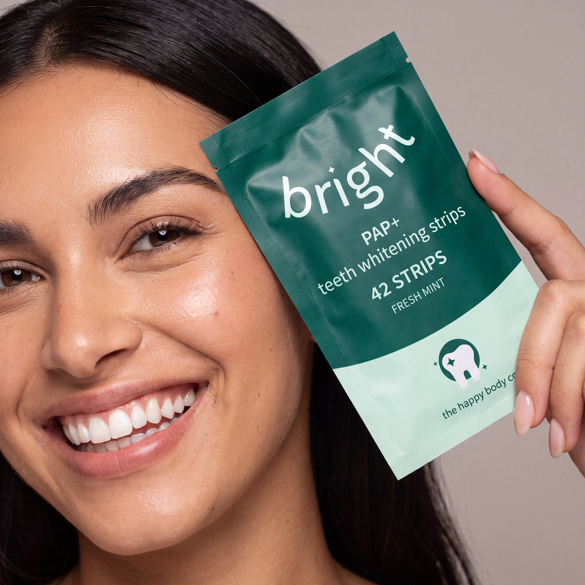 Smiling woman holding a pack of Bright PAP+ teeth whitening strips, 42 strips, fresh mint