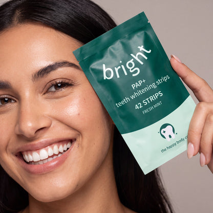 Smiling woman holding a pack of Bright PAP+ teeth whitening strips, 42 strips, fresh mint