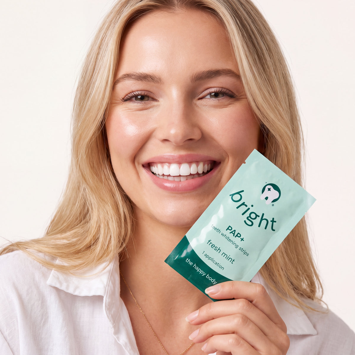 Smiling woman holding a single-application sachet of Bright PAP+ teeth whitening strips, fresh mint