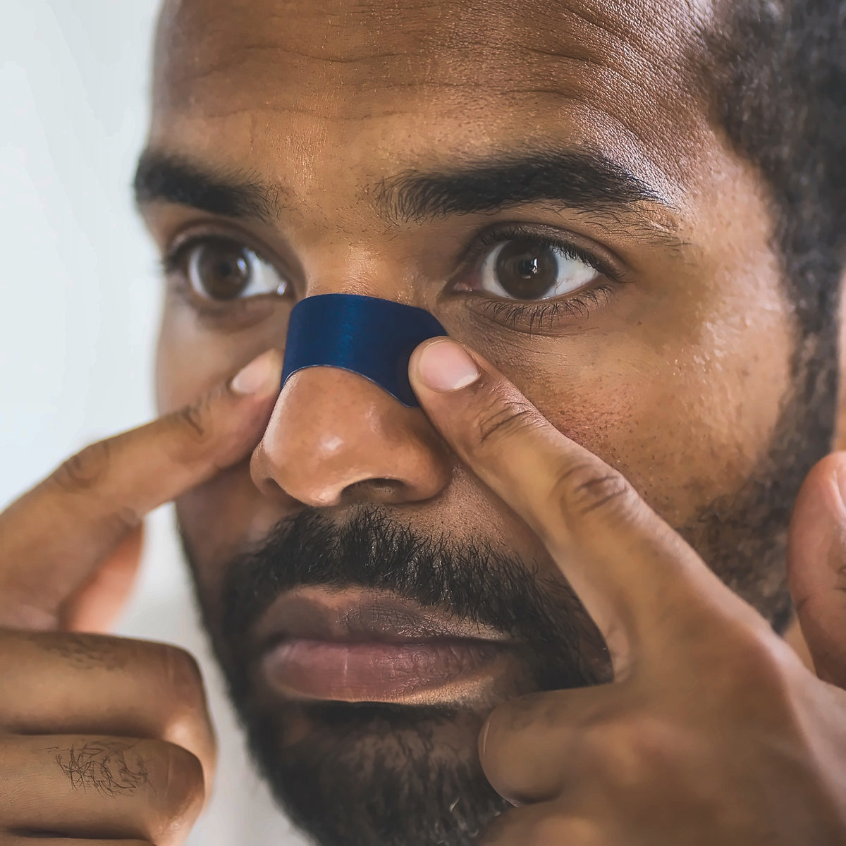 Man applying a navy Perform nose strip across the bridge of his nose