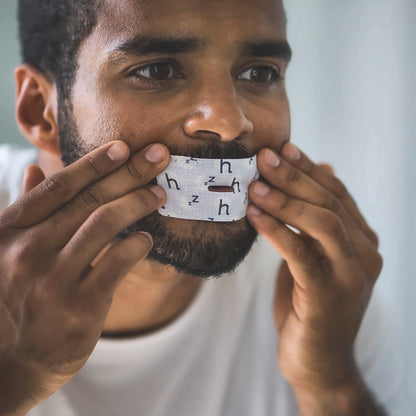 Man applying a Rest sleep tape strip over his lips, showing the central breathing vent