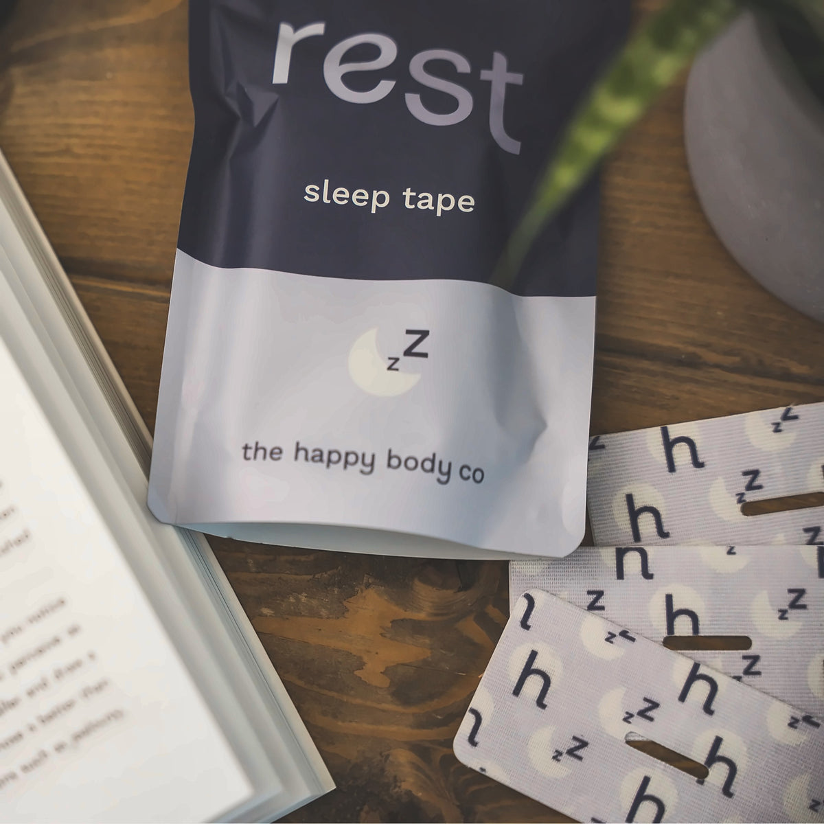 Rest sleep tape pouch and strips on a wooden bedside table next to a book